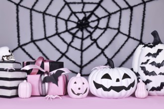 Pink and white Halloween decor with black and white pumpkins, witch hat and spell books on gray