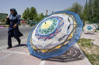 A woman walks past large umbrellas lying on the pavement in Tehran. The city of Tehran is changing