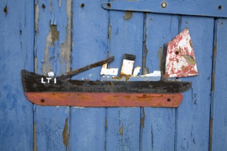 Old scrap metal model of ship on blue painted shed wall, Felixstowe Ferry, Suffolk, England, UK