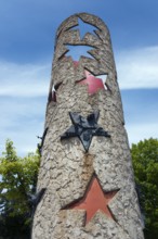 Column with punched-out stars and metal reliefs under a blue sky, National Column in front of the