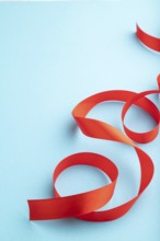 Red coral ribbon on a blue pastel background. Celebration concept. Side view, copy space