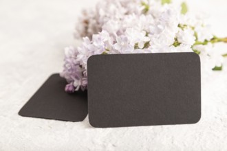 Black business card with lilac flowers on gray concrete background. side view, copy space, mockup,