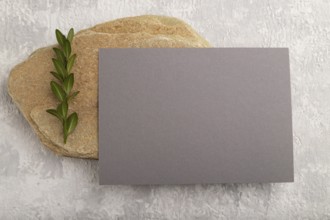 Gray paper business card, mockup with natural stone and boxwood branch on gray concrete background.