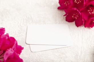 White business card with purple azalea flowers on gray concrete background. side view, copy space,