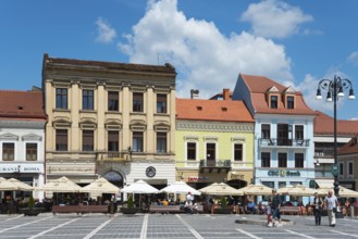 Lively city market square with street cafés and strolling passers-by, town houses on the market