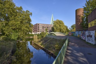 River Bocholter Aa with footpath, trees and pedestrian bridge under a cloudless blue sky in