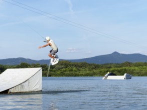 Sporty young man with wakeboard, jump over obstacle, jump, water sports, water skiing and wake