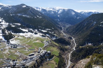 Bergtal mit einem Fluss, grünen und verschneiten Flächen und einer Straße, die sich durch das Tal