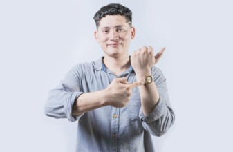 Smiling young man pointing at his wrist watch isolated. Portrait of person pointing his wrist watch