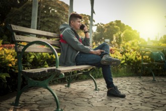 Man sitting on a bench calling on the phone, young man sitting on a bench with cell phone, close up