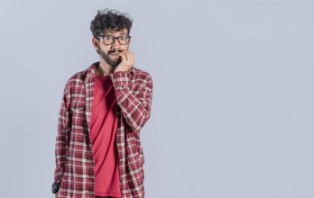 Nervous young man with worried expression bites nails and looks anxiously isolated