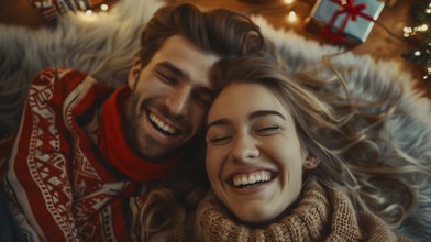 Young couple laying on their backs surrounded by christmas gifts and decorations laughing.