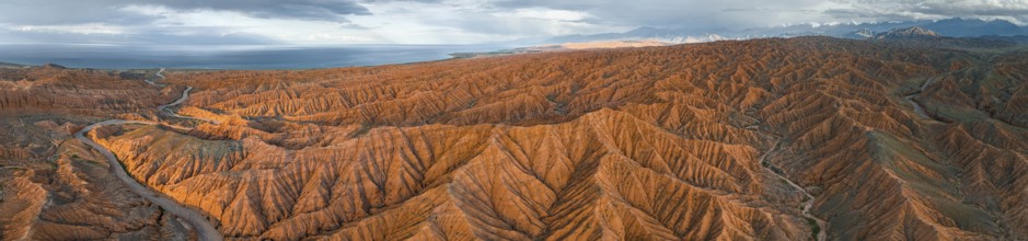 Panorama, landscape of eroded hills, badlands at sunset, behind mountain peaks of the Tian Shan