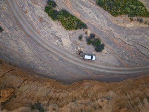 Off-road vehicle on a track in a riverbed, landscape of eroded hills, top-down, badlands, aerial