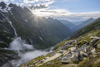 Atmospheric mountain landscape, clouds forming in a mountain valley in the evening light, sun star,