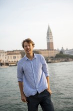 Young man in striped shirt and shorts on the banks of the Grand Canal, looking into the camera,