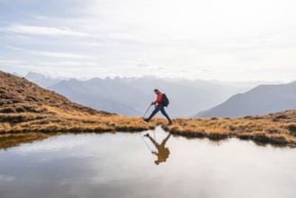 Mountaineer hiking with poles, reflected in a small mountain lake on the Krahberg, mountain