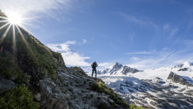 Mountaineer in front of high alpine mountain landscape with sun star, summit of Aiguille de