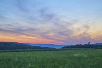 Green field with trees in the background under a dramatically illuminated sunset, the sky is bathed