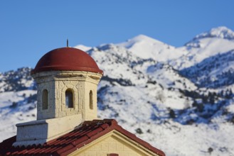 Close-up of a church tower with a red roof in the snowy mountains under a clear sky, Lefka Ori,