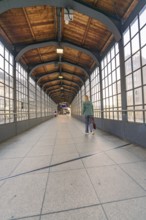 A covered pedestrian bridge in a railway station with glass windows and wooden ceiling, Berlin,