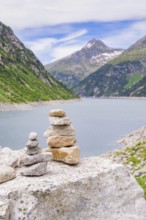 Mountain landscape with a calm lake and a pile of stones in the foreground, surrounded by green