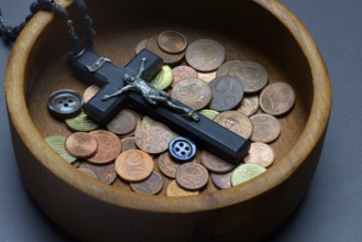 Crucifix with coins and buttons in a wooden bowl, church and money