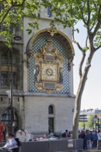 Magnificent golden clock on an ornate wall of a large building with passers-by, Paris