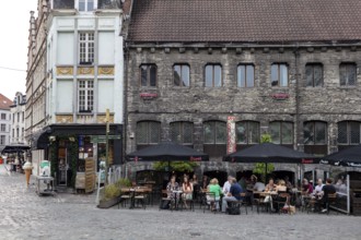 People sitting in a street café next to an old building with cobblestones, Ghent