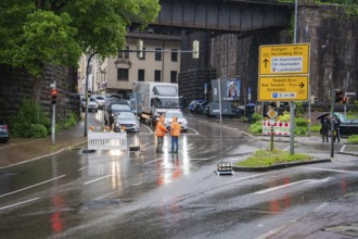 Road closure due to construction site in the city during rain, workers and traffic signs visible,