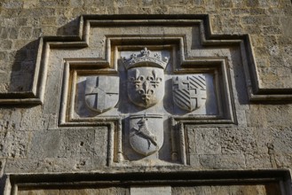 A coat of arms carved into a stone wall with various historical symbols, Knights' Street, Rhodes