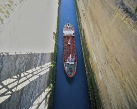 Aerial view of a red ship travelling through a narrow channel under a bridge, Corinth Canal,