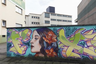 Woman with flowers in her hair, coloured mural in front of industrial building, graffiti,