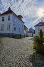 A quiet cobbled street in Bergen's old town centre, with traditional houses and sunny summer