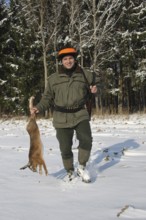 Hunter with hare (Lepus europaeus) in the snow, on the way to the assembly point, Lower Austria,