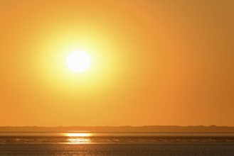 Sunset over the North Sea at low tide, the outline of the island of Juist on the horizon,