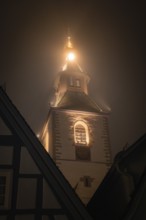 A church tower at night, shrouded in thick fog and illuminated by warm lights, Old Tower, Nagold,