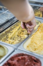 A hand scoops yellow ice cream out of a metal box with an ice cream scoop, Autumn creations at Cafe