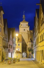 Galgengasse and White Tower in the old town of Rothenburg ob der Tauber, illuminated at night.