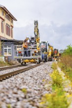 Rail vehicles and workers in a construction environment with houses and plants, track construction