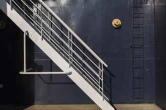 White painted metal stairs and black ladder against blue metal wall on a cruise ship, La Spezia,