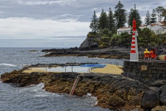 Small lighthouse and seawater swimming pool on the rocky coast under a cloudy sky, Caloura fishing