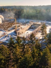 Construction site in the snow, surrounded by trees and a construction crane, under a clear sky, new