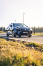 Black car driving on a road with meadow, bright sun in the background, e-car sharing vehicle of