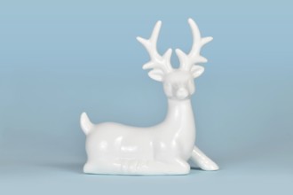 White ceramic Christmas or winter decoration deer figurine on light blue background