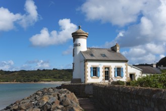 Coastal scene with lighthouse and cottage, surrounded by rocks and with blue sky and clouds,