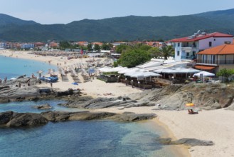 Beach with umbrellas and beach houses, clear blue water and mountains in the background, Sarti,