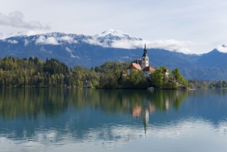 Church on an island, reflected in the calm lake, with mountain scenery in the background, Bled