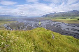 Hiker, young man on a hill, view over alluvial land, meandering river, Dímonarhellir, Suðurland,