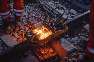 Worker during night-time track work with welding equipment and red-hot melting point on the rails,